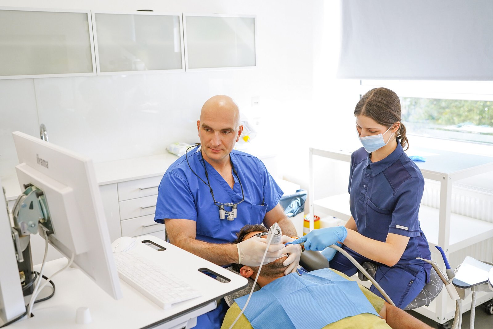 Zwei Behandler versorgen einen Patienten, die digitale Planung ist am Bildschirm sichtbar